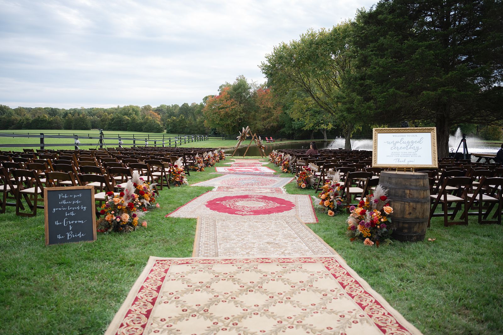 The ceremony site at the pond with vintage rugs down the aisle and fall florals on the arch