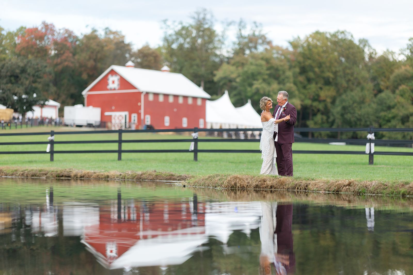Shannon and Brian by the pond with the red barn and sailcloth tent behind them