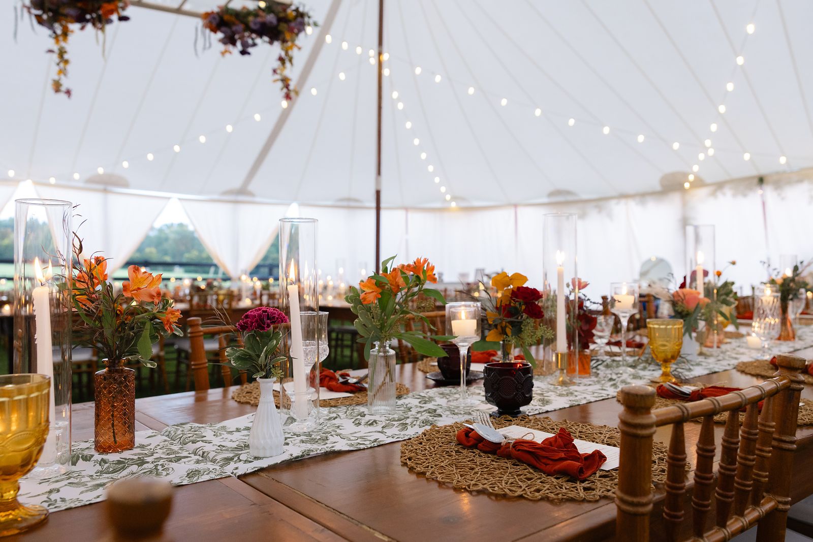 Inside the sailcloth tent with string lights, long wooden tables, and fall florals