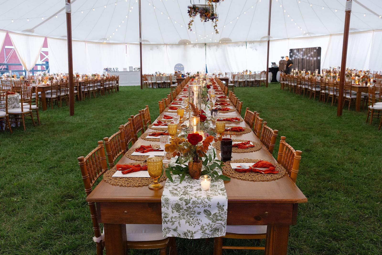 Long farm tables with orange and burgundy florals in the reception tent