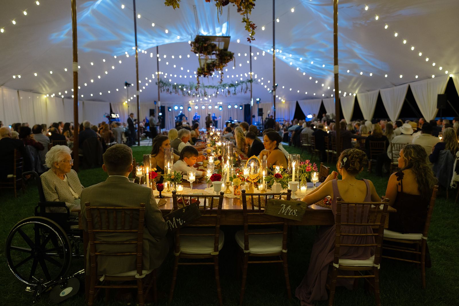 Wide view of the reception tent at dusk with string lights and floral chandelier